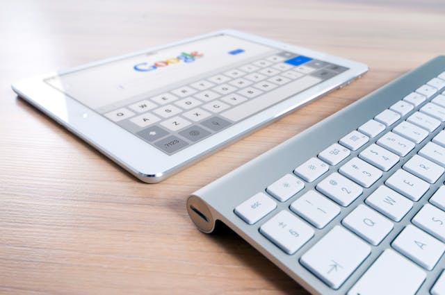 A white tablet displaying the Google homepage with SEO optimization for therapy websites lies next to a silver keyboard on a wooden desk.